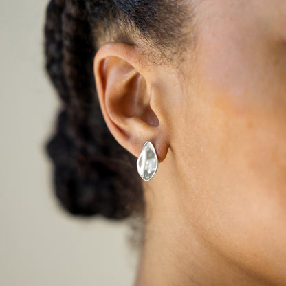 Close-up of an ear wearing a silver petal earring with blurred background
