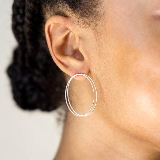 Close-up of an ear wearing a silver hoop earring with blurred hair and background