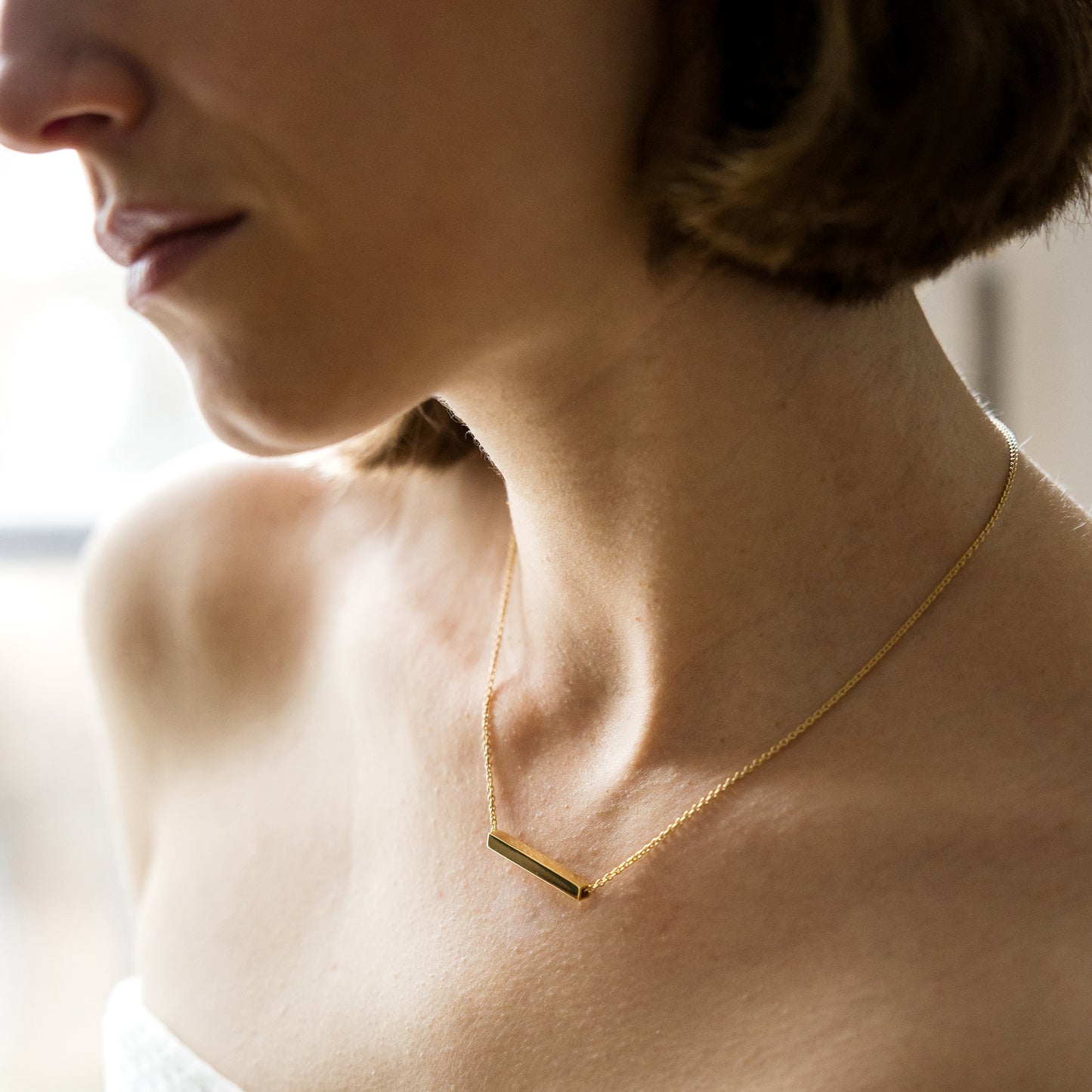 Close-up of a person wearing a gold necklace with a bar pendant.
