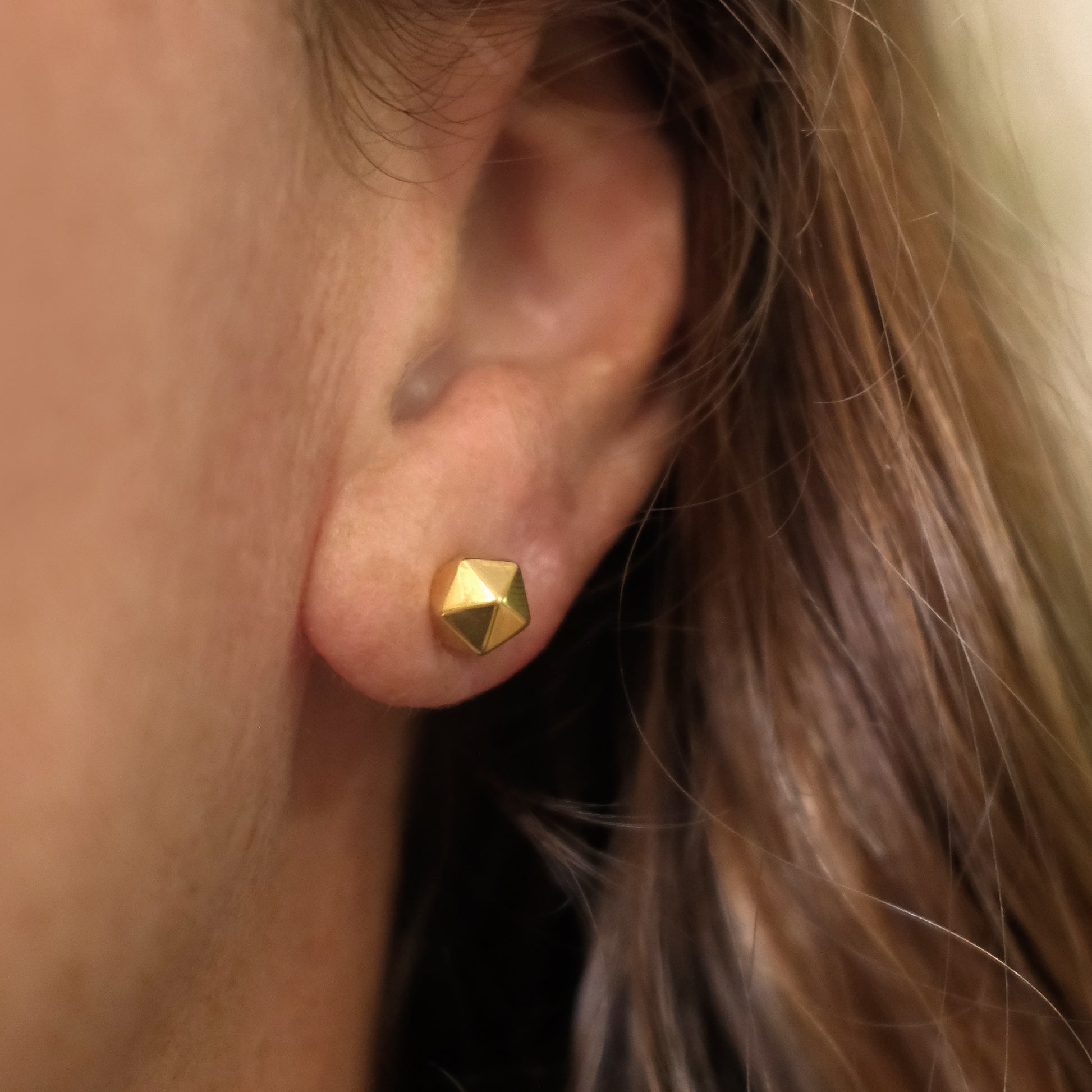 Close-up of an ear wearing a gold geometric stud earring.