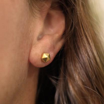 Close-up of an ear wearing a gold geometric stud earring.