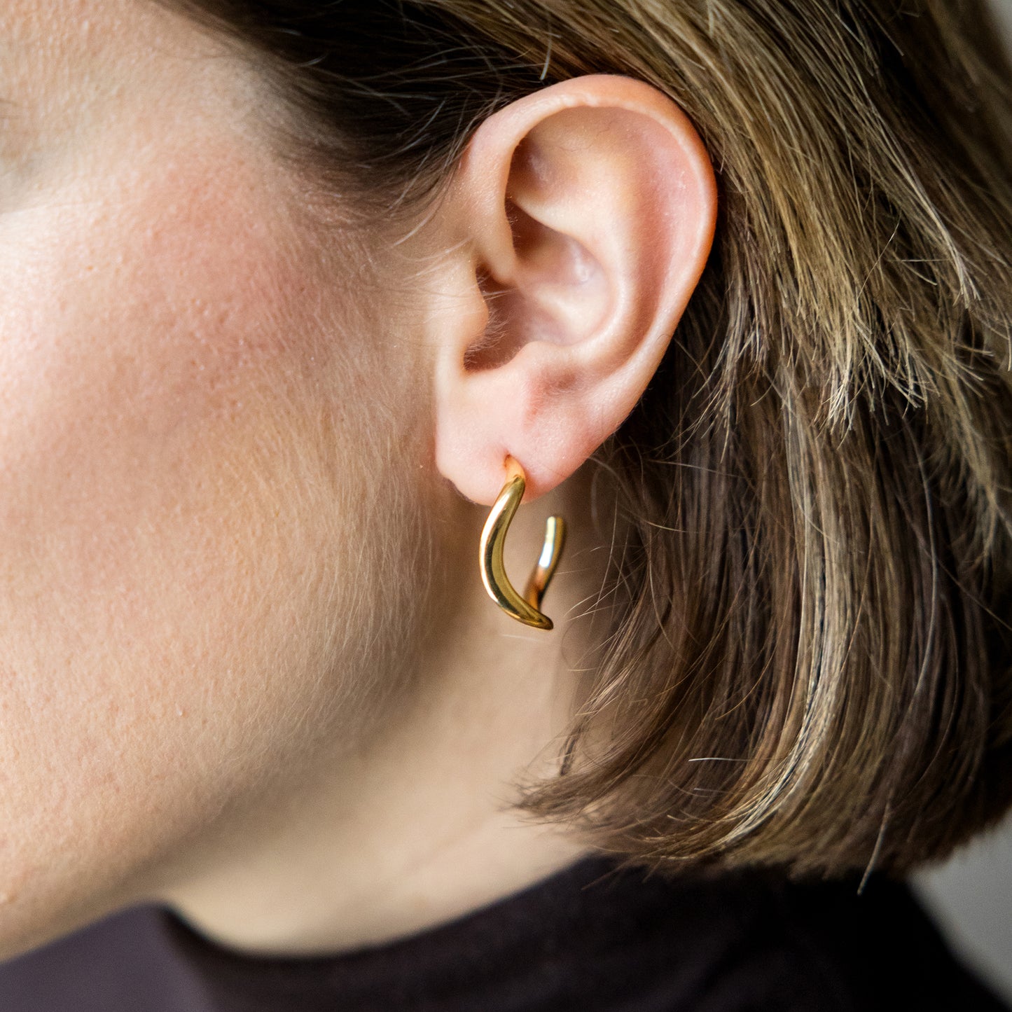 Close-up of a person wearing a gold hoop earring.