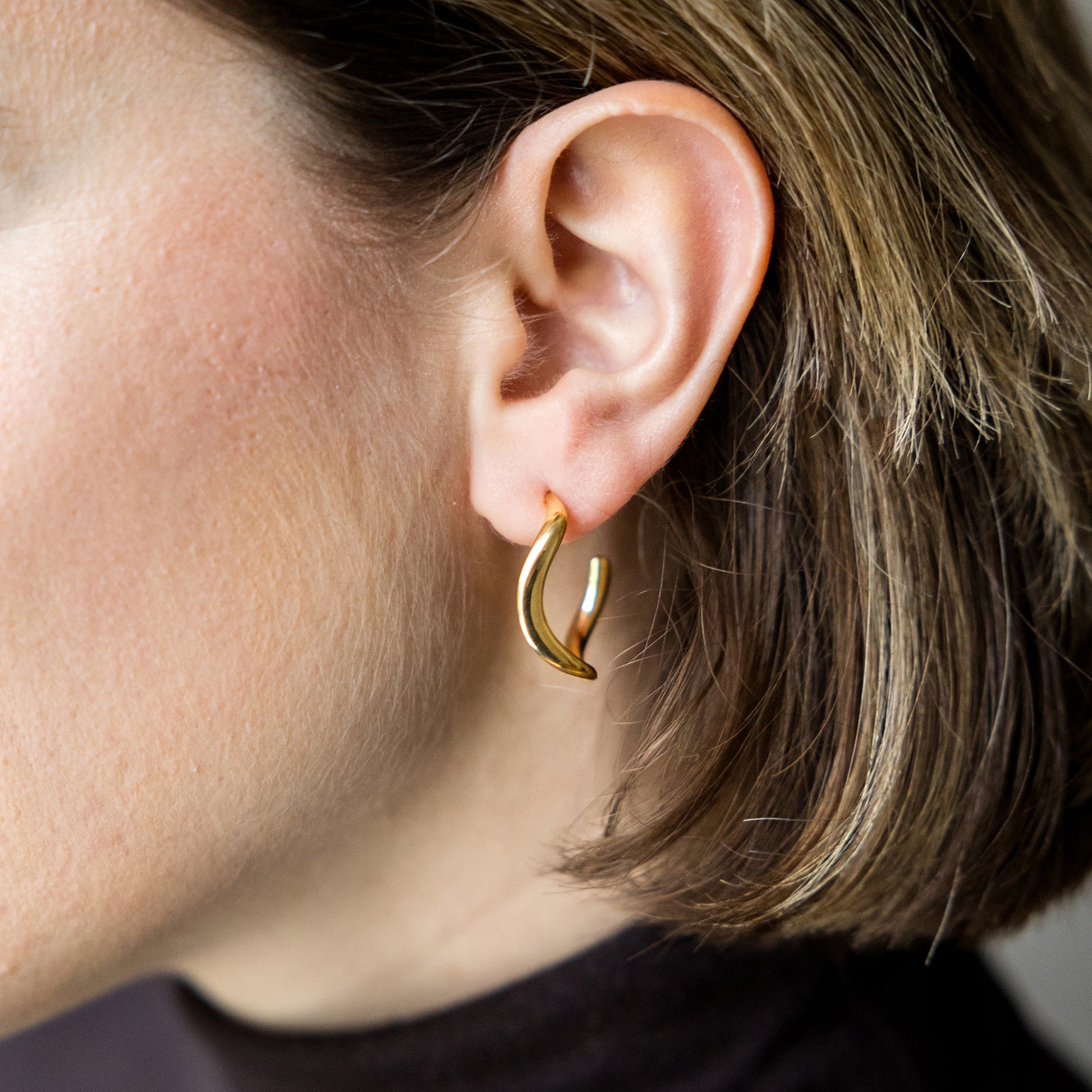 Close-up of a person wearing a gold hoop earring.