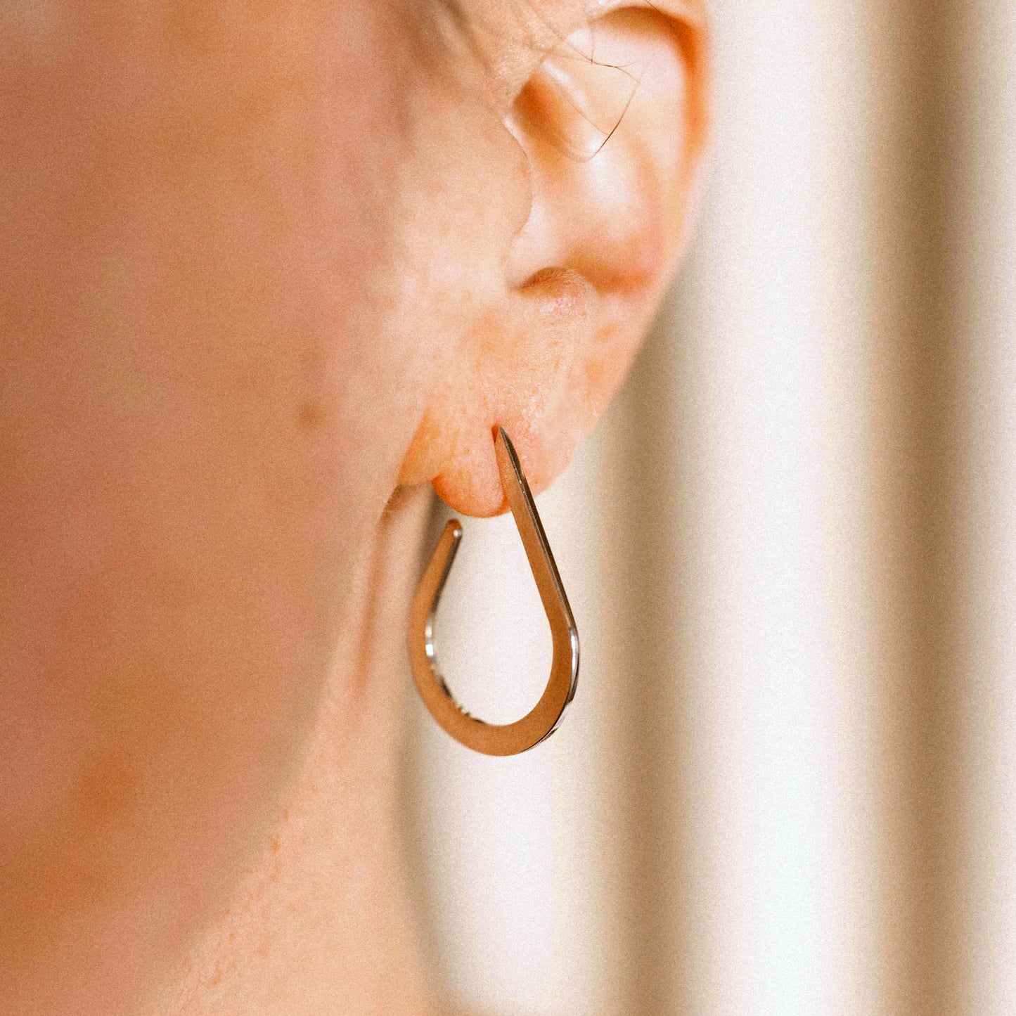 Gold hoop earring worn by a person with a neutral background