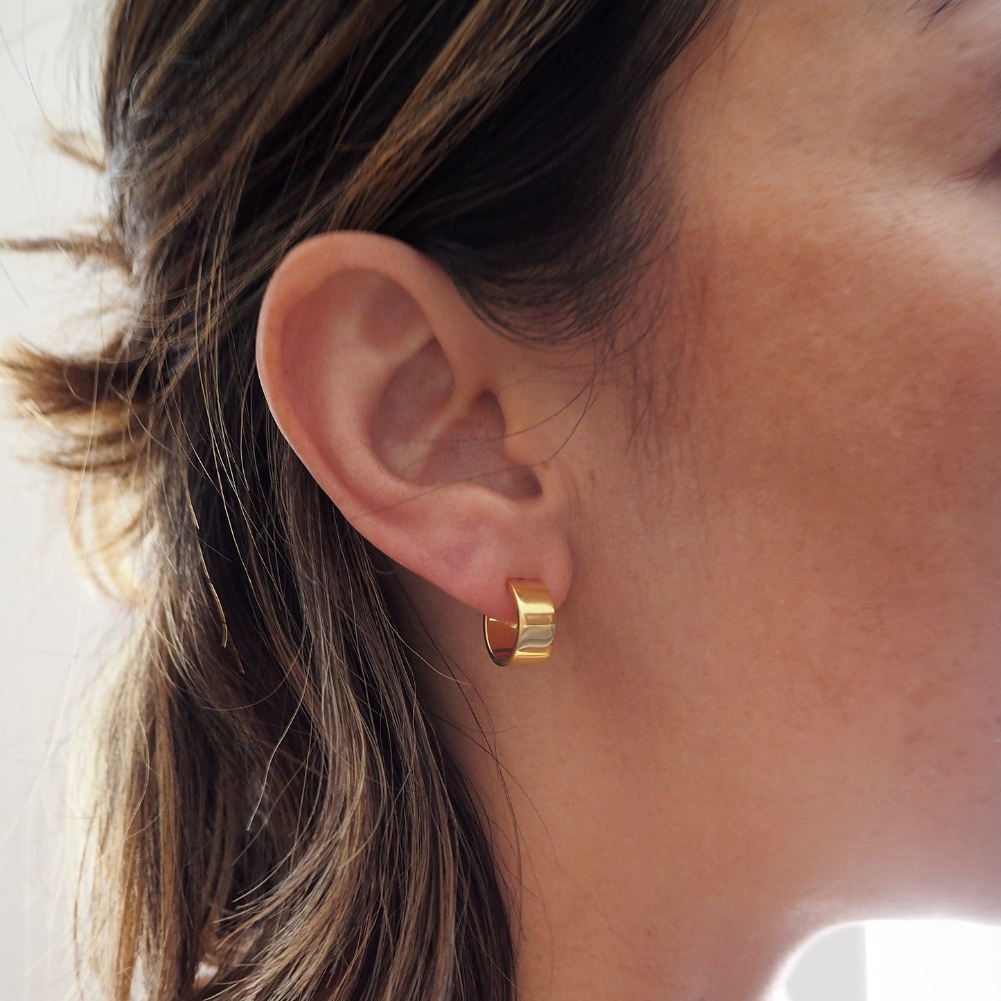 Close-up of a person wearing a gold hoop earring with a neutral background