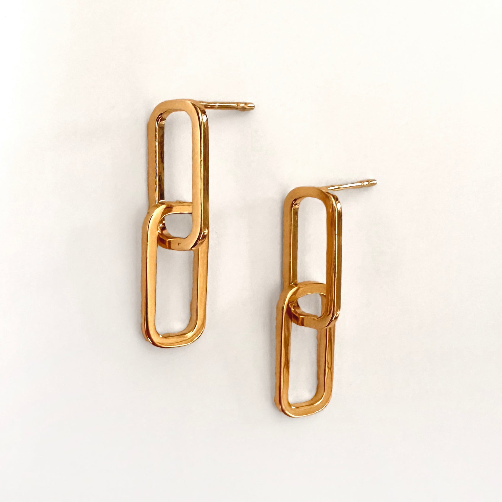 A pair of gold linking oval earrings against a white background