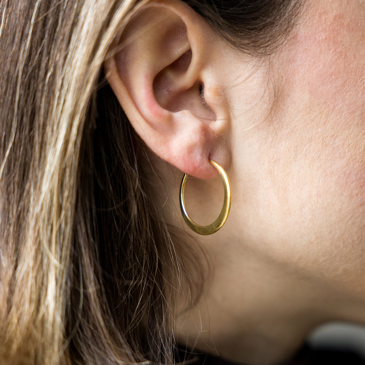 Close-up of a person wearing a gold hoop earring.