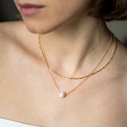 Close-up of a person wearing a delicate gold necklace with a pearl pendant.