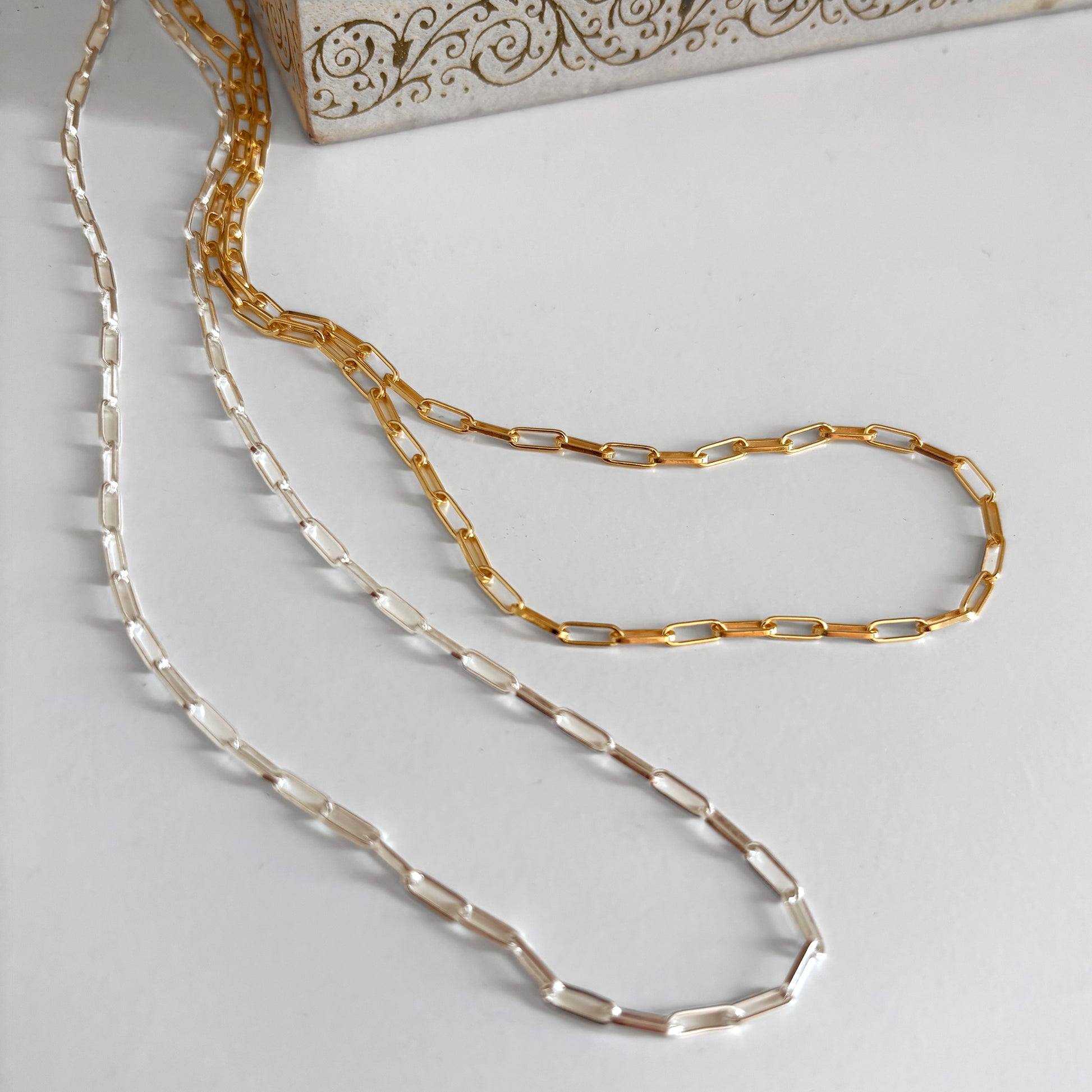 Gold and silver chain necklaces on a light gray surface