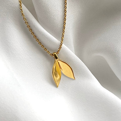 Gold necklace with a leaf-shaped pendant on a white fabric background