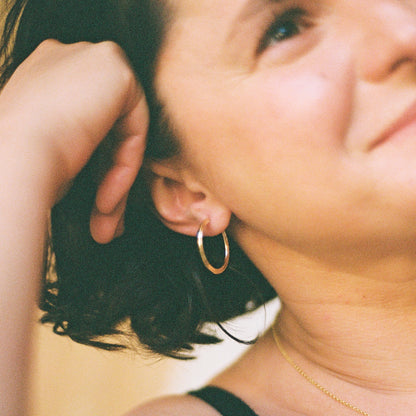 Close up of a person wearing a gold hoop earring against a blurred background