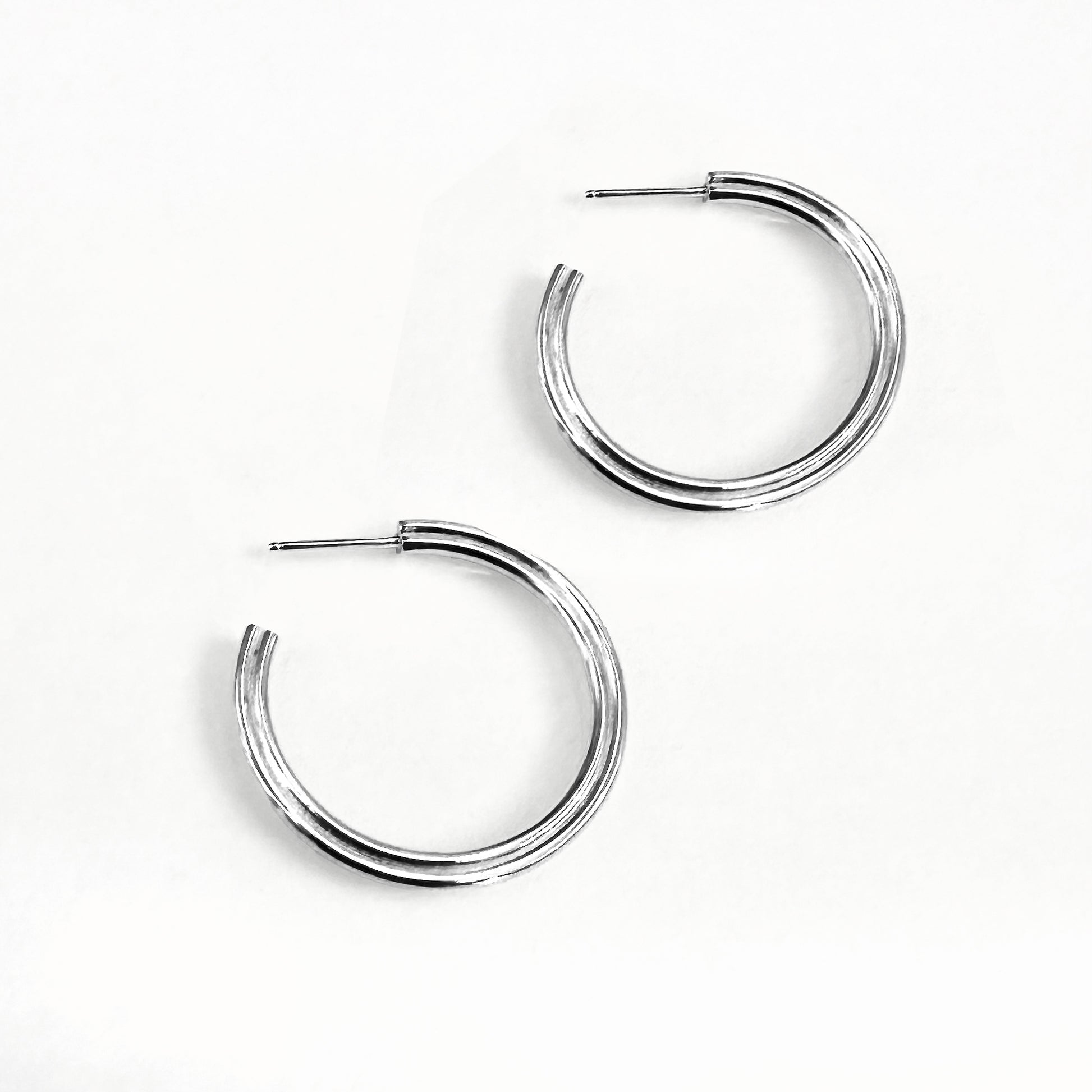 A pair of silver hoop earrings with a subtle heart shape design, viewed from the side