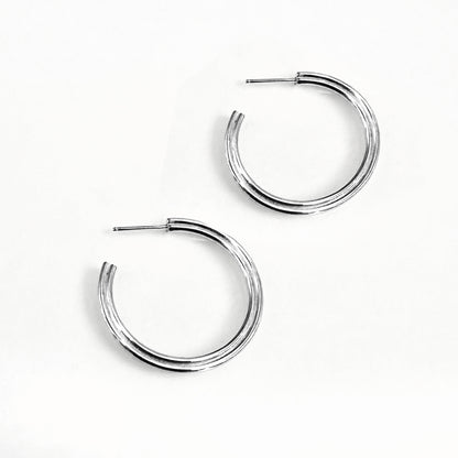 A pair of silver hoop earrings with a subtle heart shape design, viewed from the side