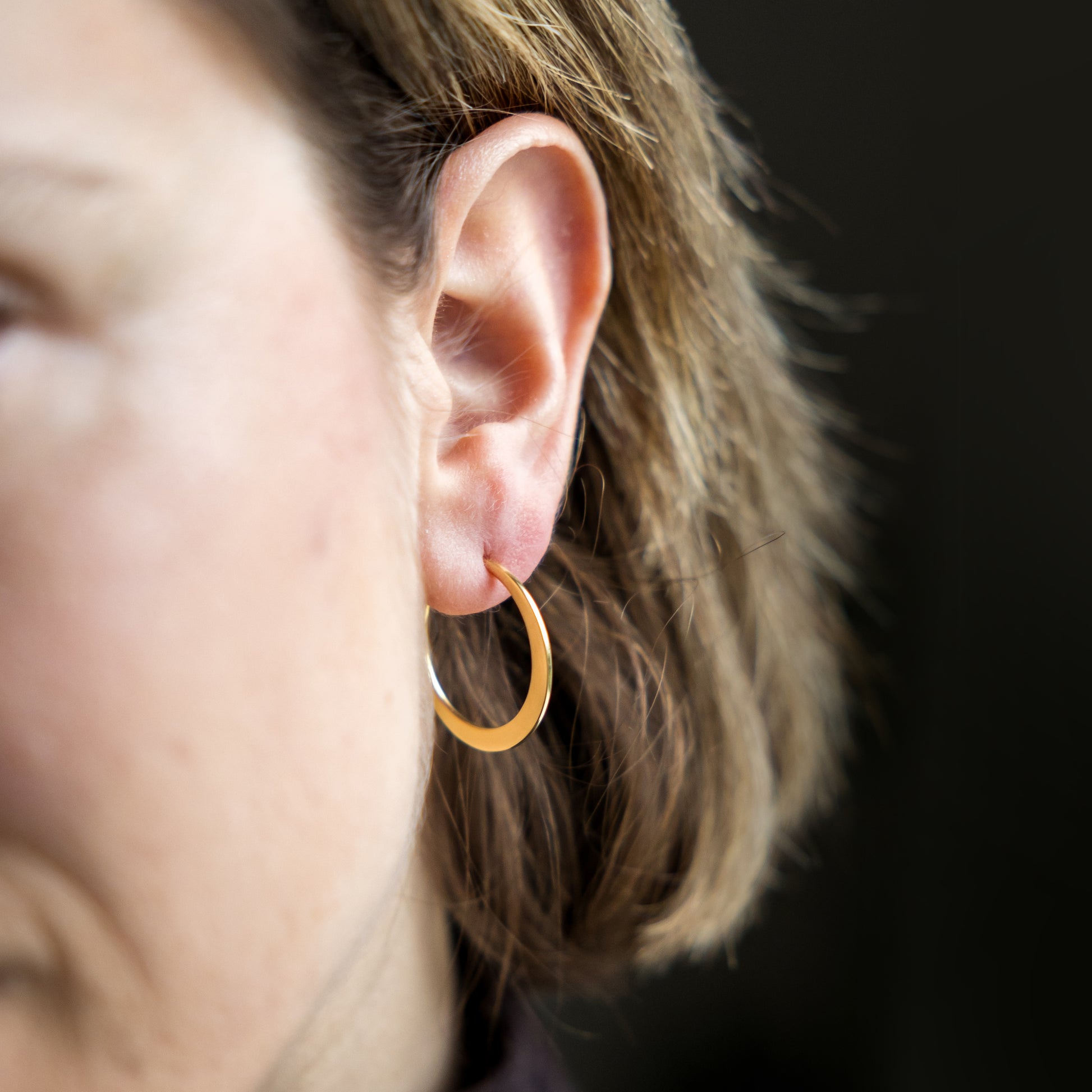 Close-up of an ear wearing a gold hoop earring with a blurred background
