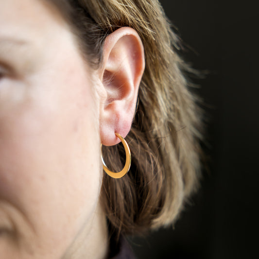 Close-up of an ear wearing a gold hoop earring with a blurred background