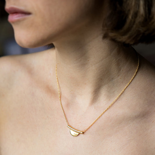 Close-up of a person wearing a gold necklace with a pendant.