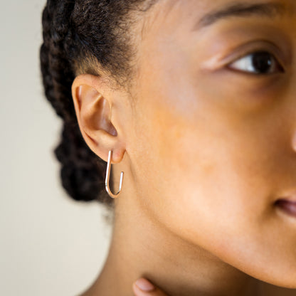 Close-up of a person wearing a silver hoop earring with a neutral background