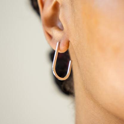 Silver hoop earring worn by a person with a neutral background