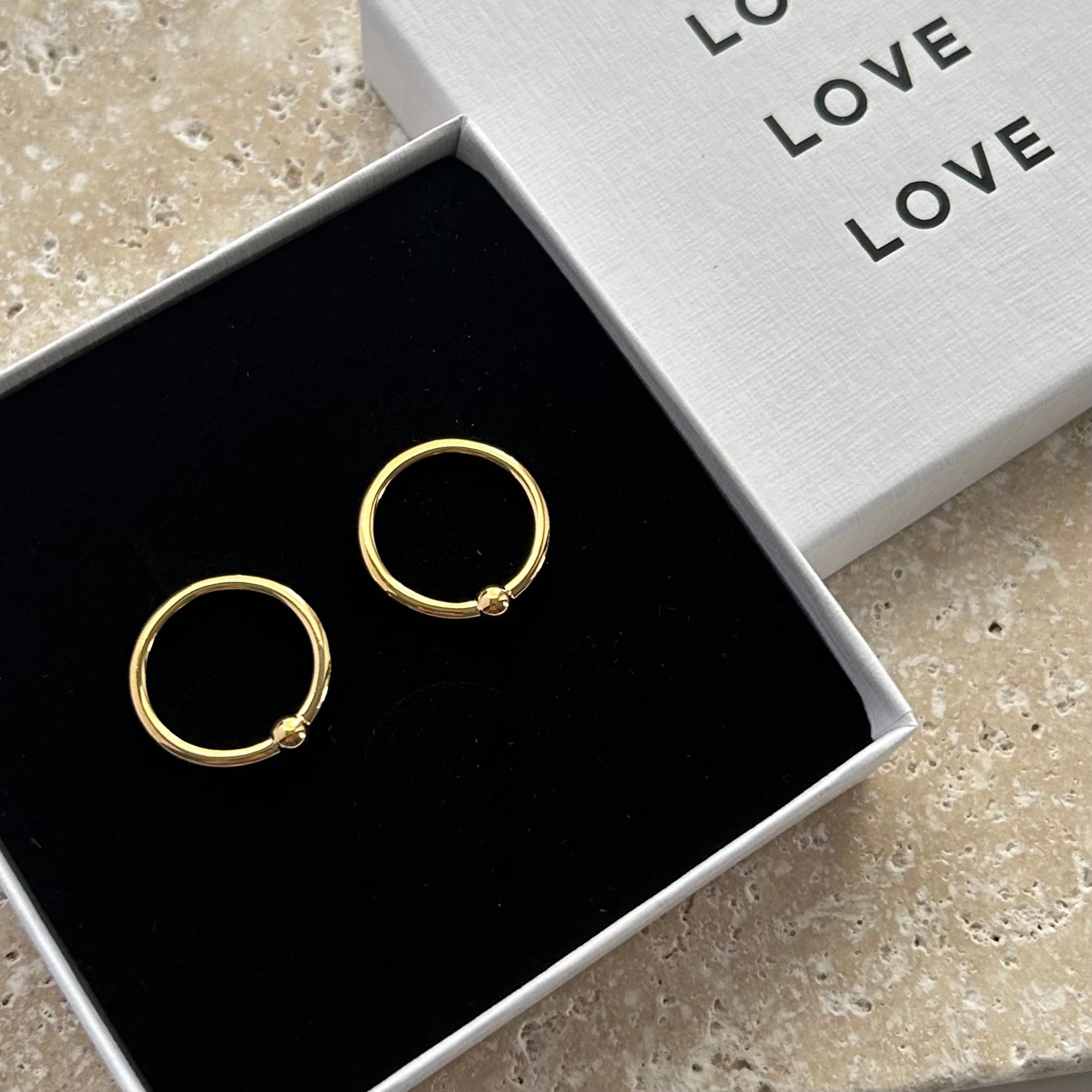 Gold hoop earrings in a box with 'LOVE' text on a stone surface