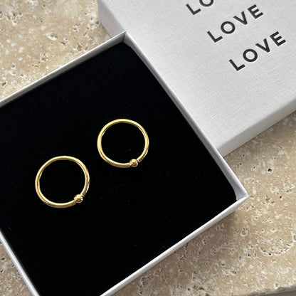 Gold hoop earrings in a box with 'LOVE' text on a stone surface