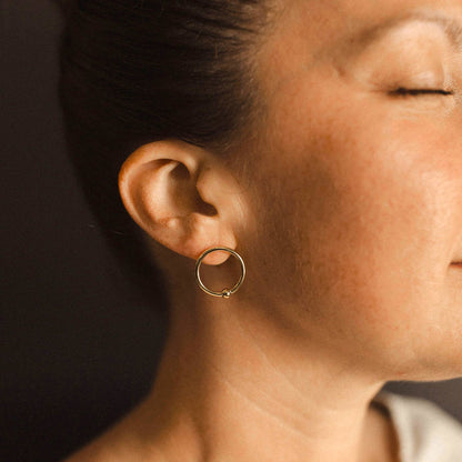 Close-up of a person wearing a gold hoop earring with eyes closed.