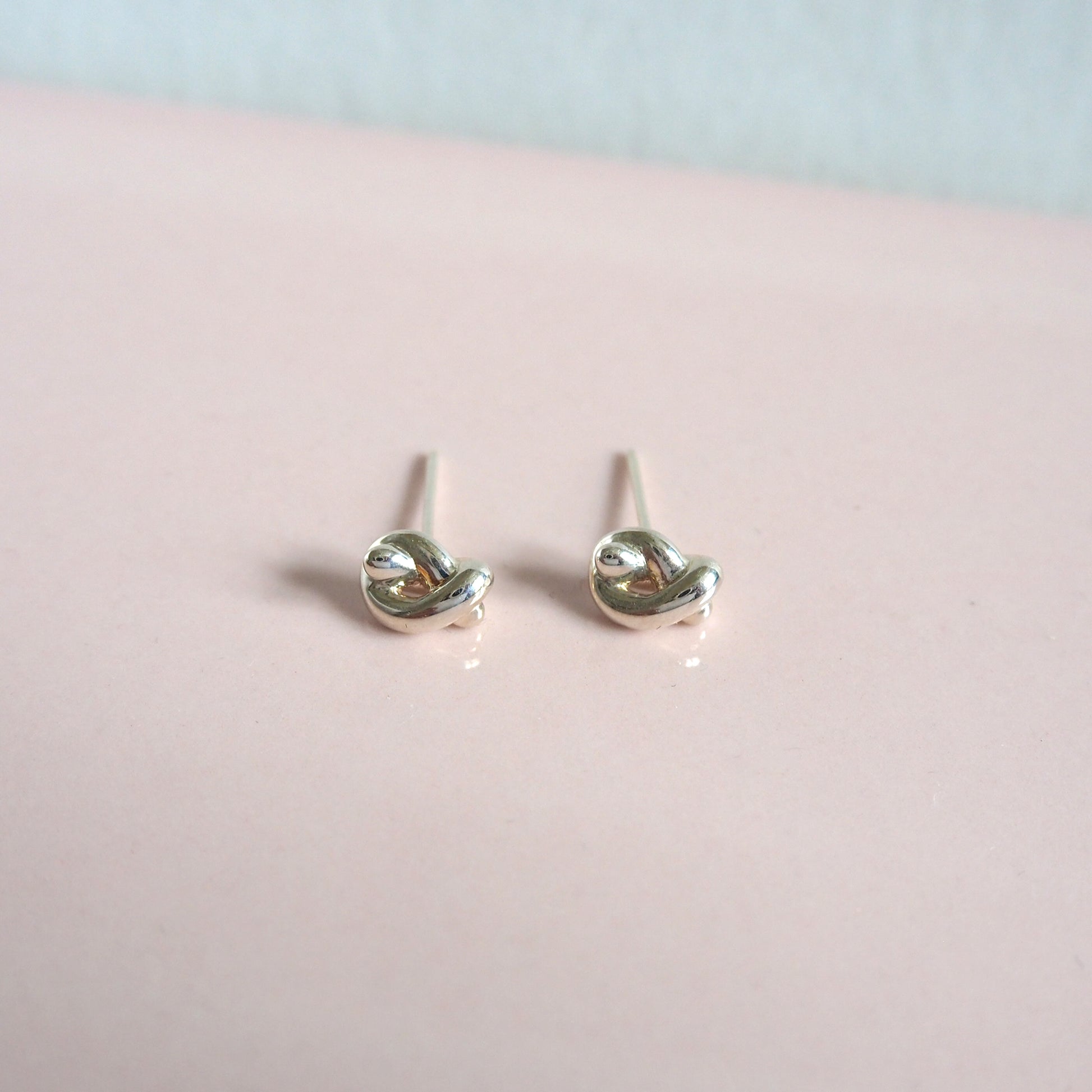Silver knot-shaped earrings on a pink surface with a light blue background
