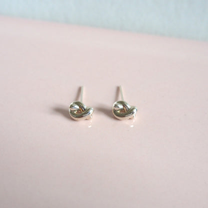 Silver knot-shaped earrings on a pink surface with a light blue background