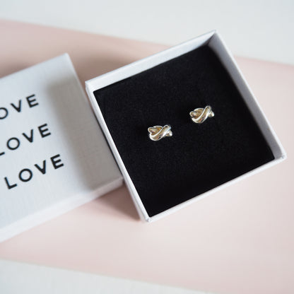 Silver knot-shaped earrings in a box with 'LOVE' text on a light background