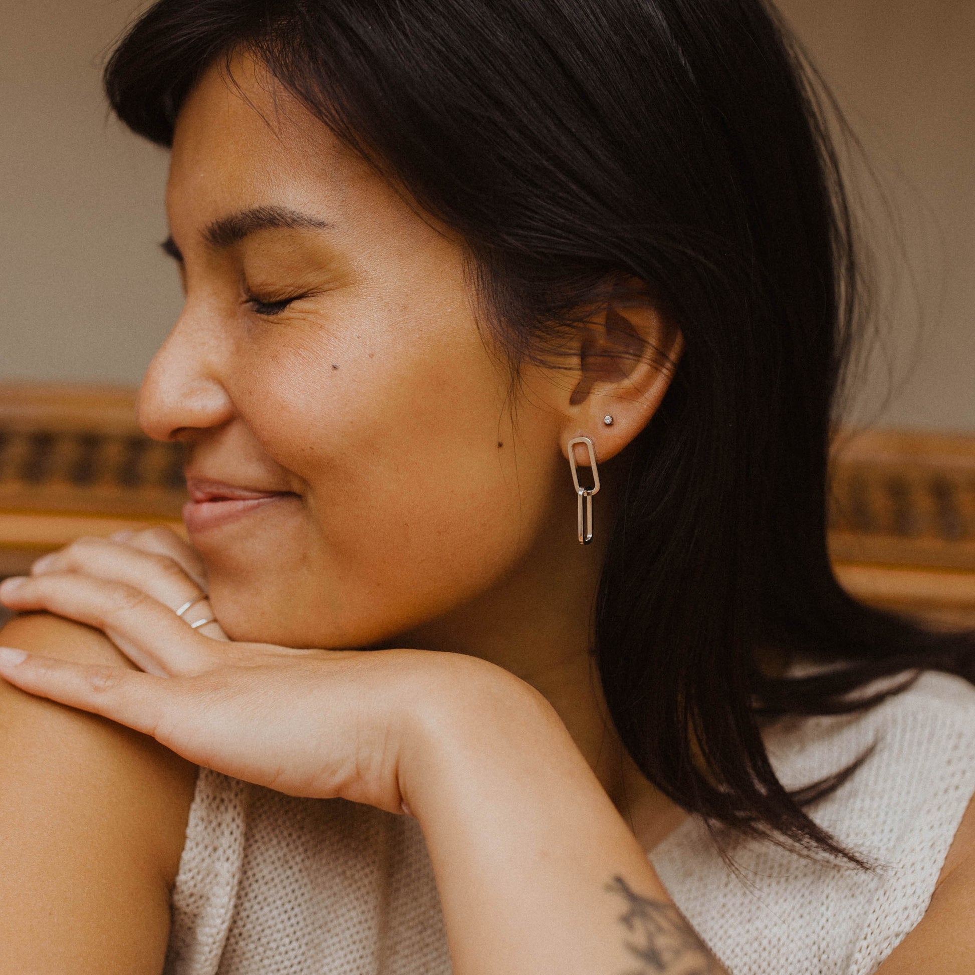 Person wearing gold linking oval earrings in front of a neutral background