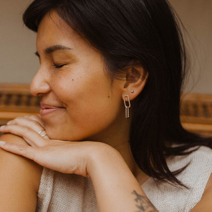 Person wearing gold linking oval earrings in front of a neutral background