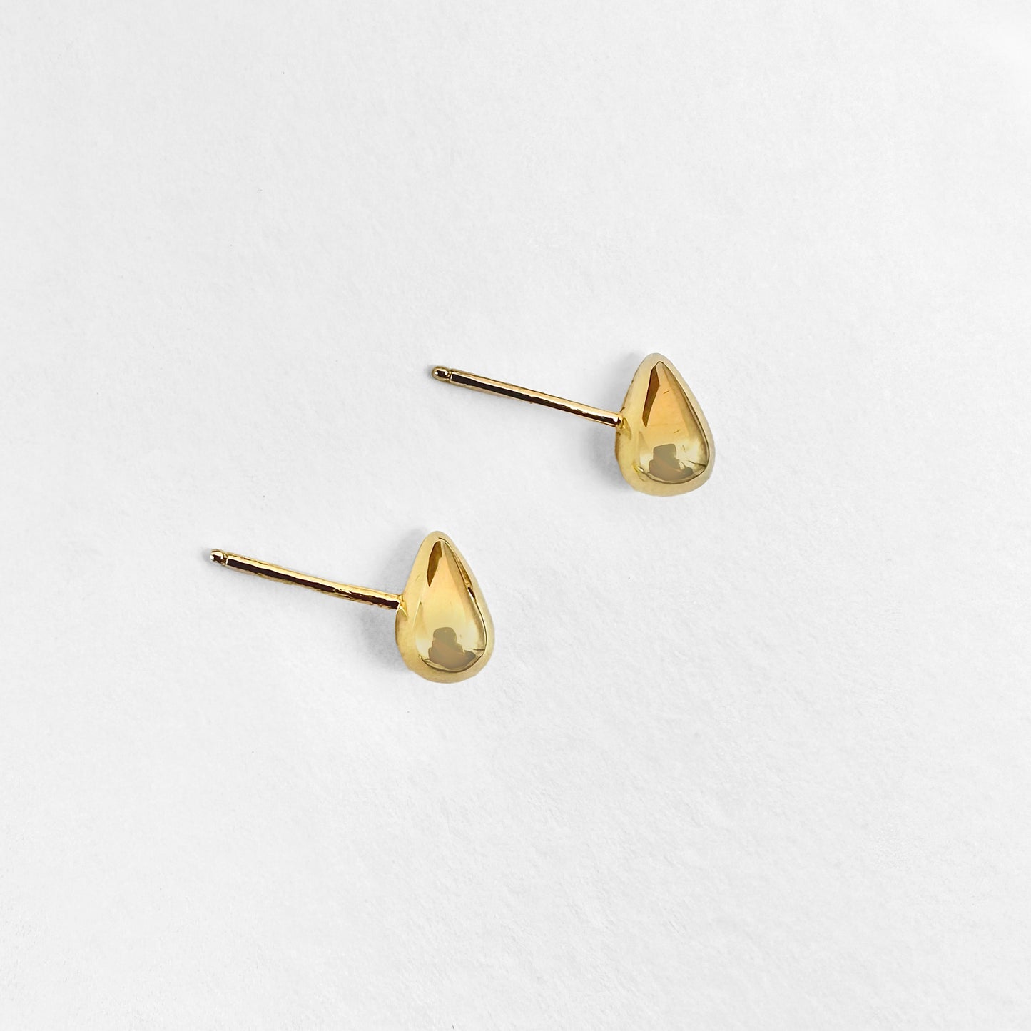 A pair of small gold water droplet stud earrings displayed against a white background.