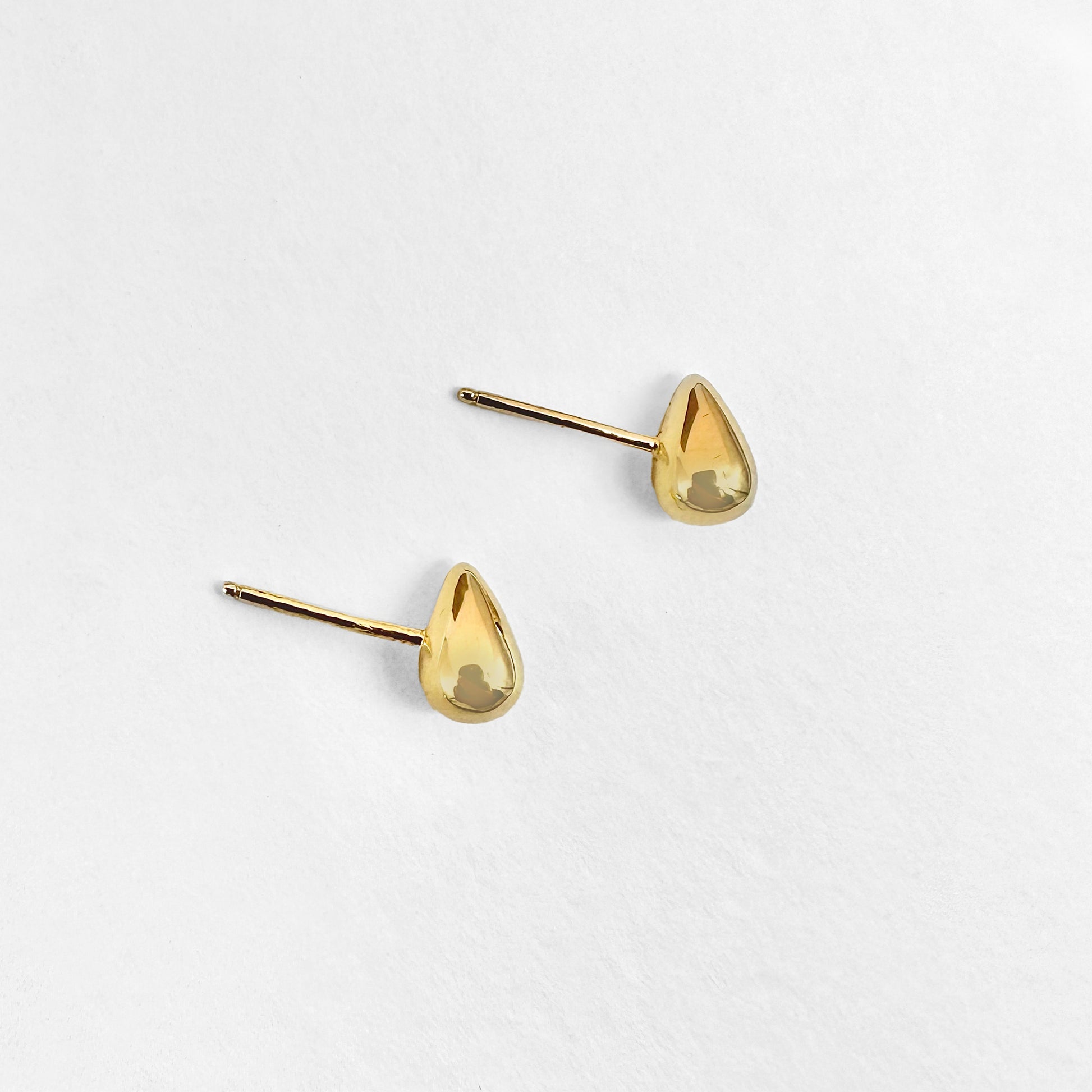 A pair of small gold water droplet stud earrings displayed against a white background.