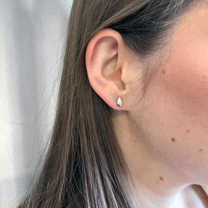 Close up of a person wearing a silver teardrop stud earring against a white background