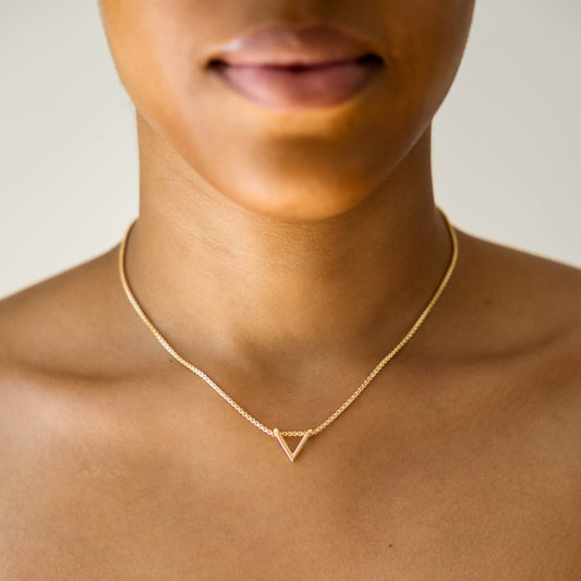 Gold necklace with a triangle pendant on a person against a neutral background