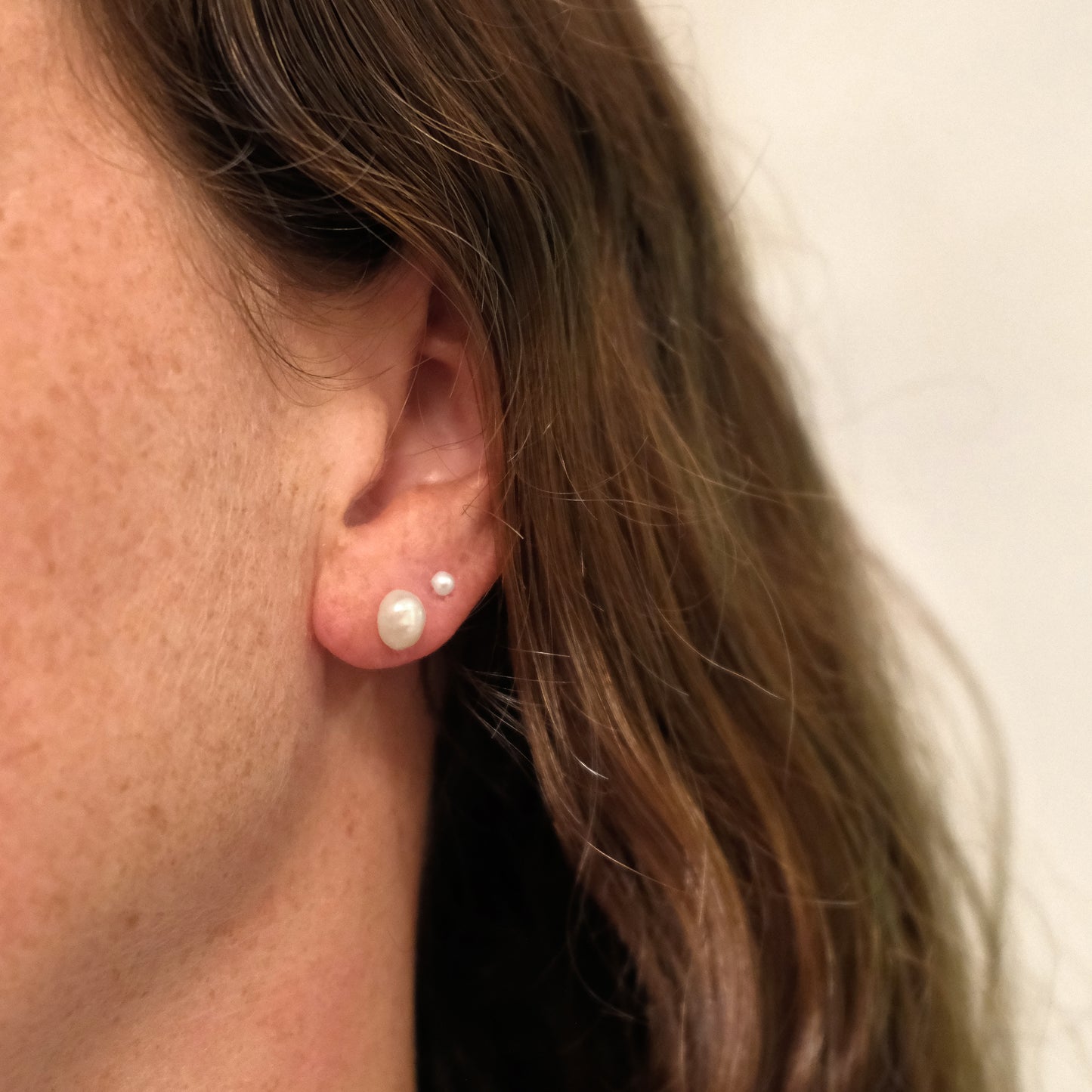 Close-up of an ear wearing pearl earrings with a neutral background