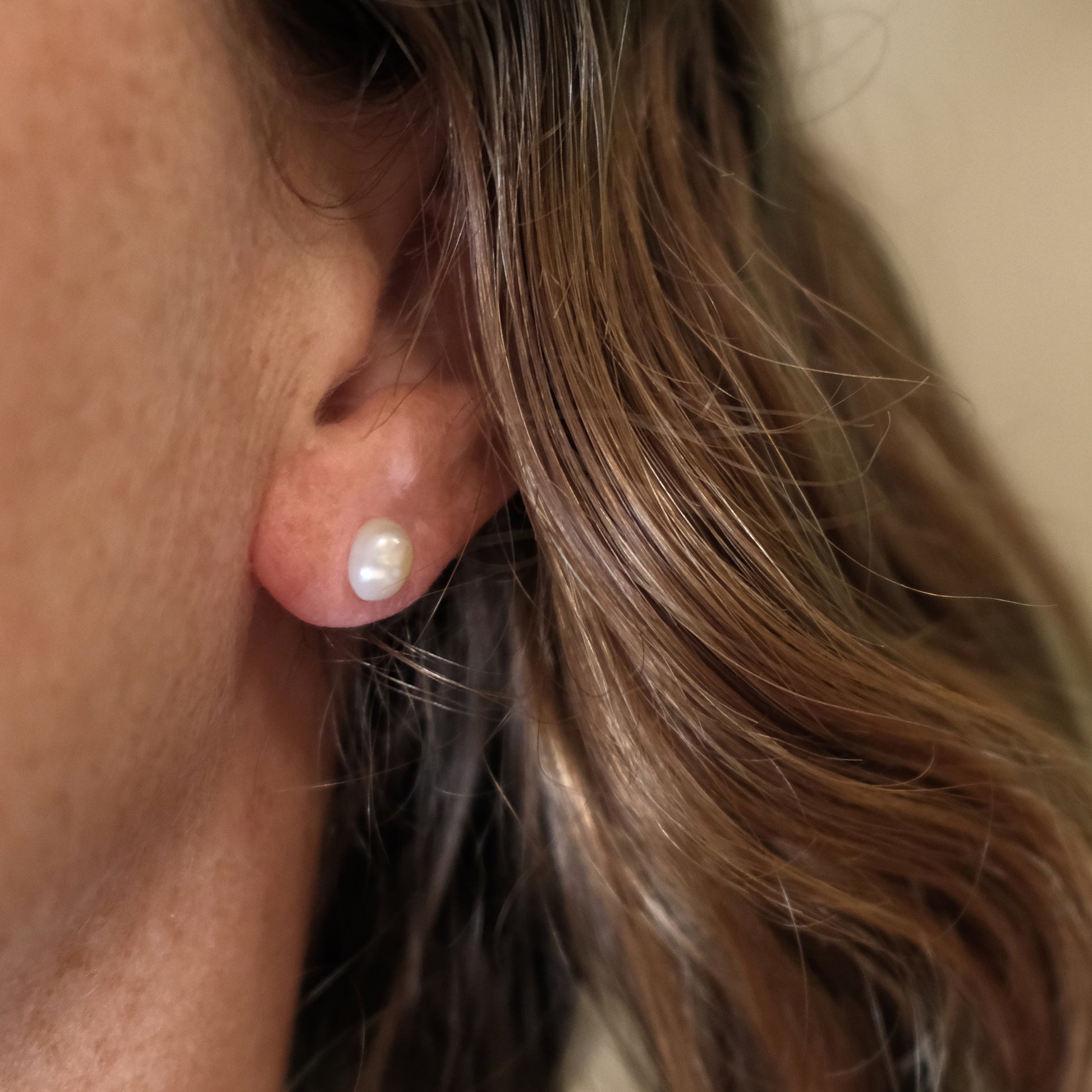 Close-up of an ear wearing a pearl earring with hair partially covering the frame.