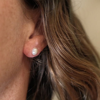 Close-up of an ear wearing a pearl earring with hair partially covering the frame.