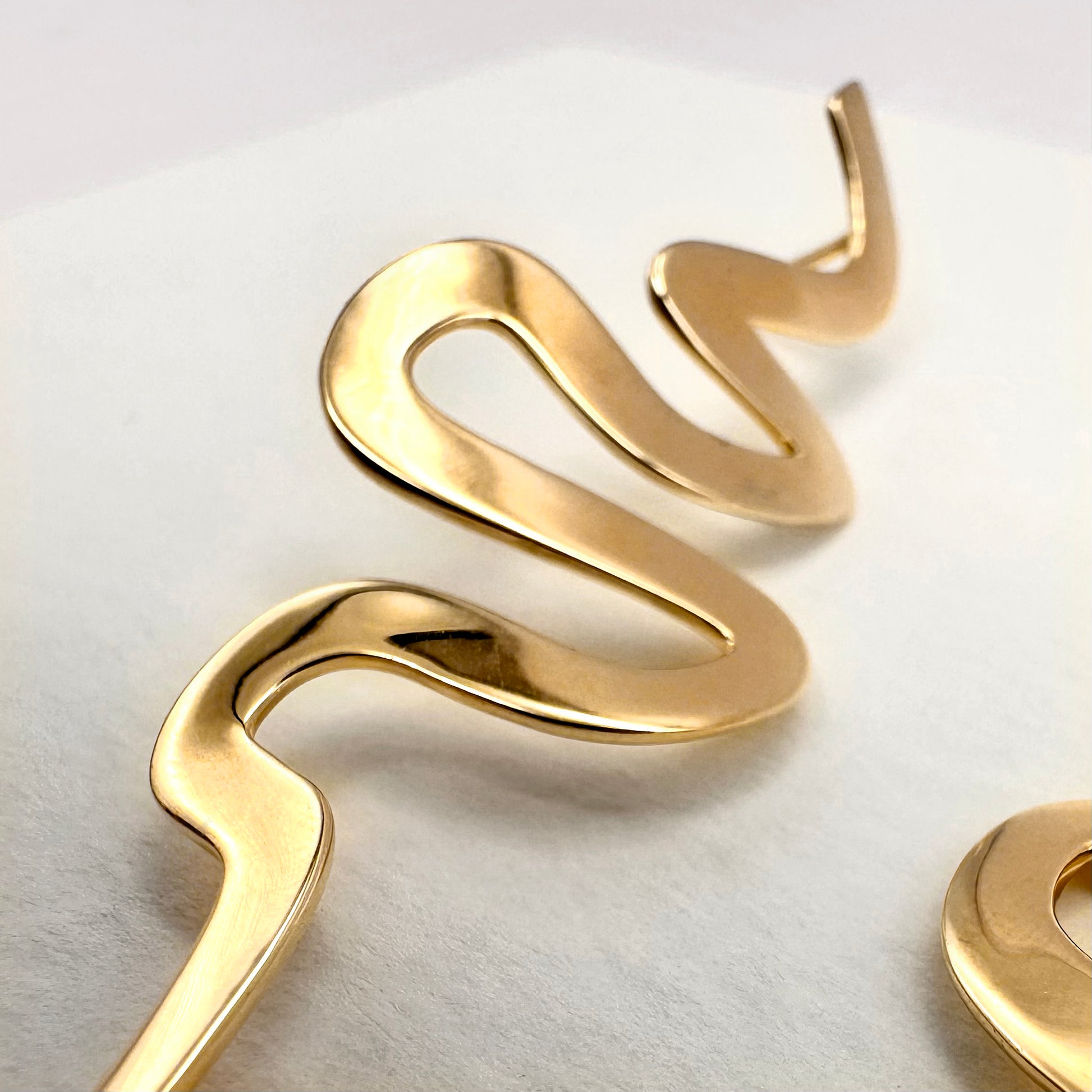 Close up of a ribbon Medusa earring on a white background
