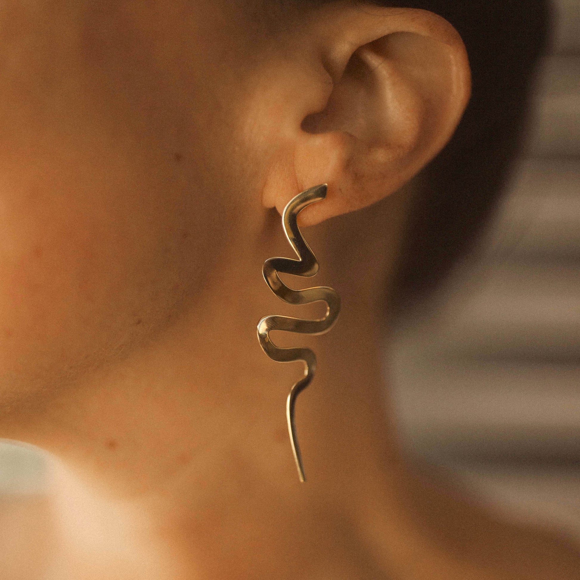 Close up of a person wearing a long snake-shaped Medusa earring
