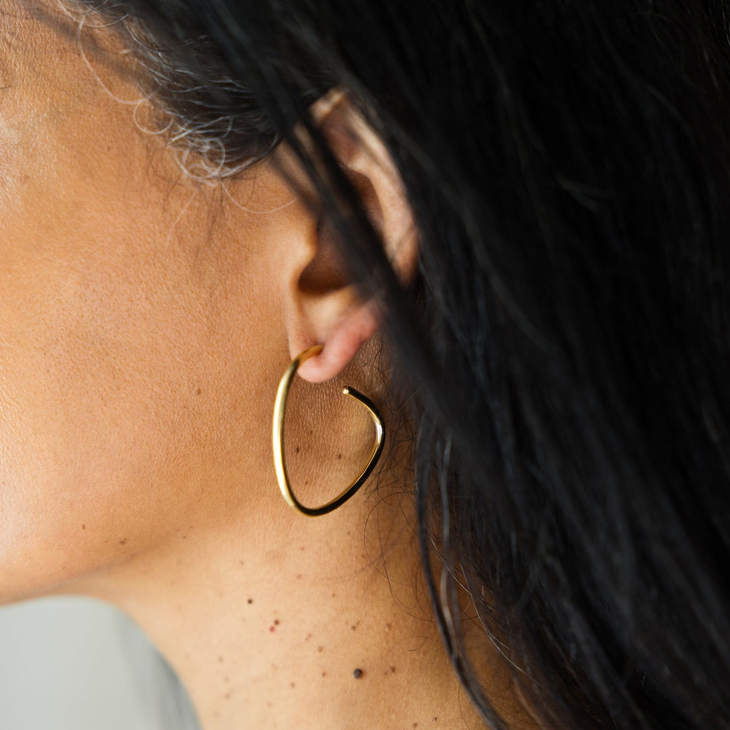 Close-up of a person wearing a gold hoop earring with dark hair and blurred background