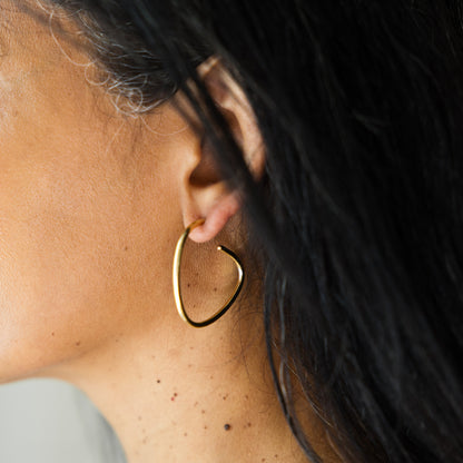 Close-up of a person wearing a gold hoop earring with dark hair and blurred background