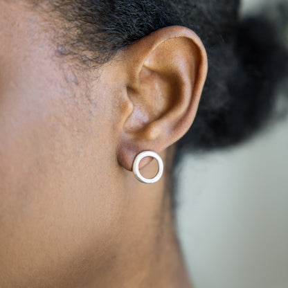 Close-up of an ear wearing a silver circular earring with blurred background