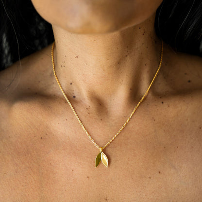 Gold necklace with a leaf pendant on a person's neck