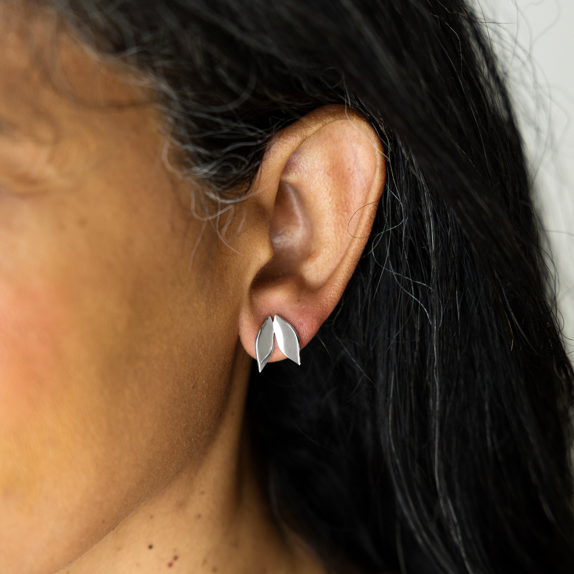 Close-up of an ear wearing a silver leaf-shaped earring with dark hair and skin background.