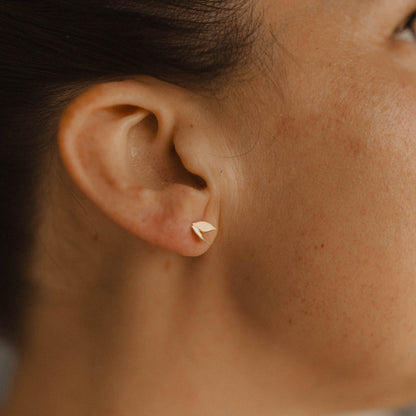 Close up of a person wearing a small gold leaf-shaped earring