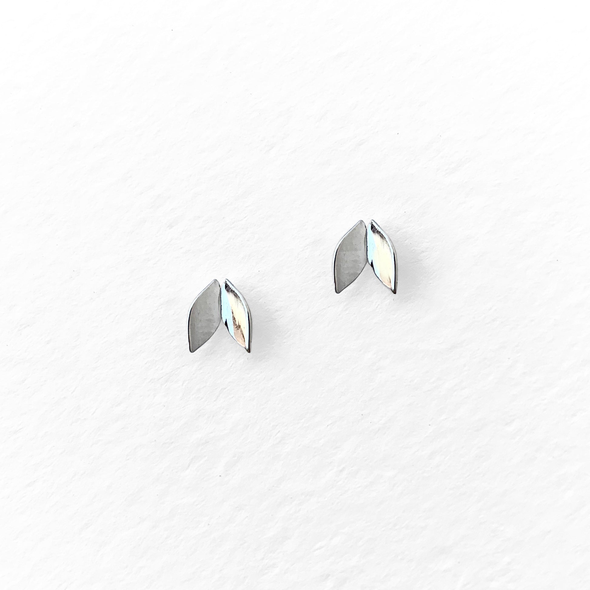 A pair of silver-colored leaf-shaped stud earrings against a white background.