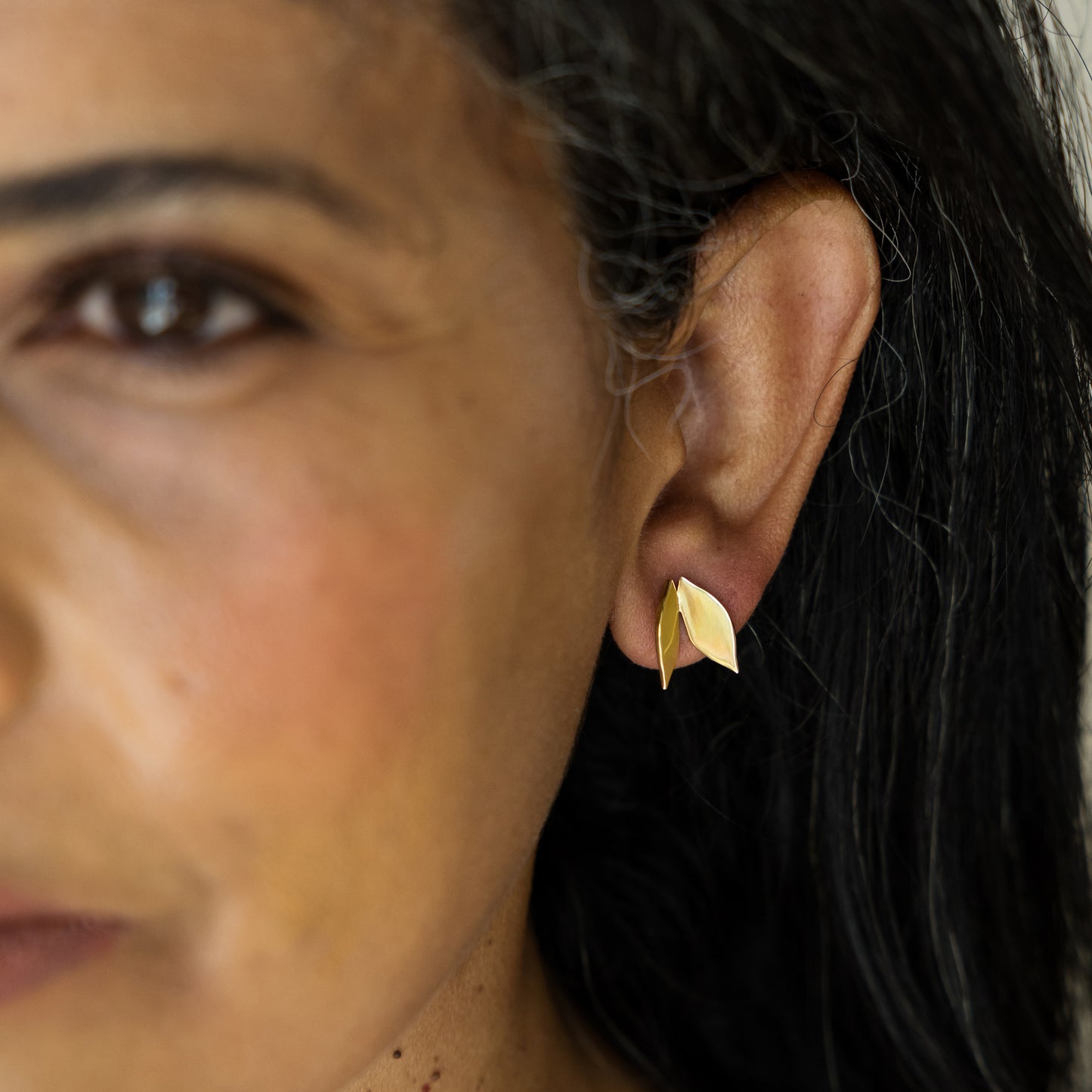 Close-up of a woman wearing a gold leaf-shaped earring.