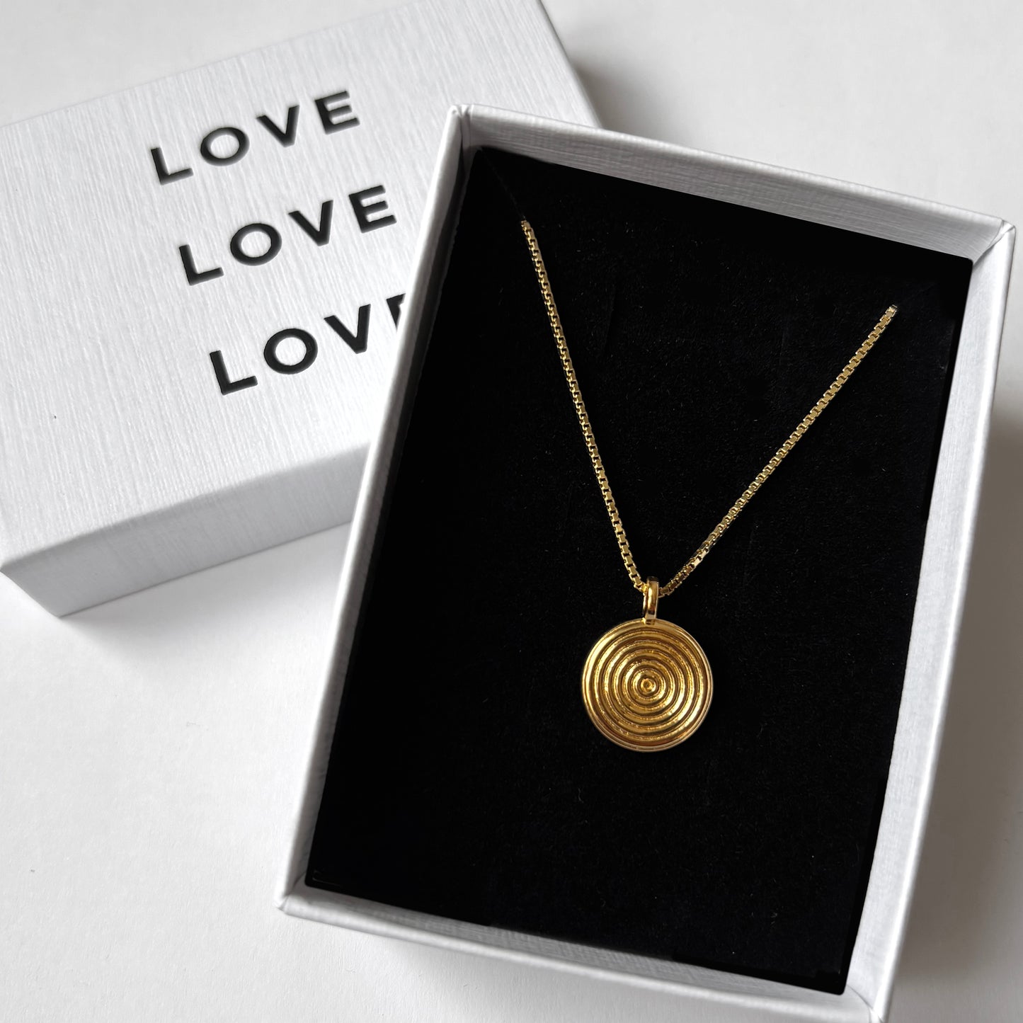 Gold necklace with a circular pendant in a box labeled 'LOVE'.