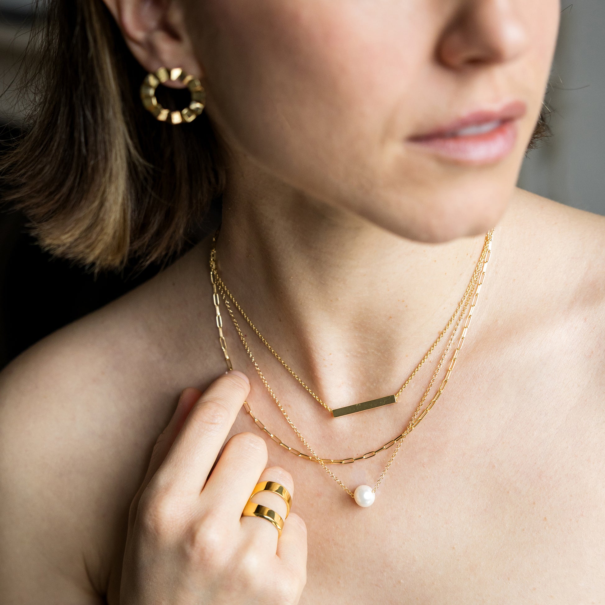 Close-up of a woman wearing gold jewelry including a necklace, earrings, and ring.