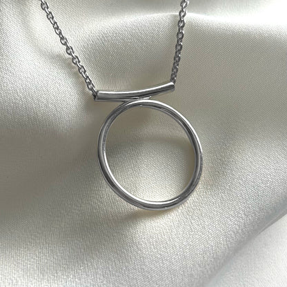 Silver necklace with a circular pendant on a light fabric background